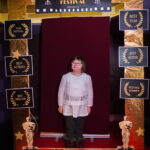dziewczyna z zespołęm downa pozuje do zdjęcia, przed nią złota rama z napisem "Cinema Festival"