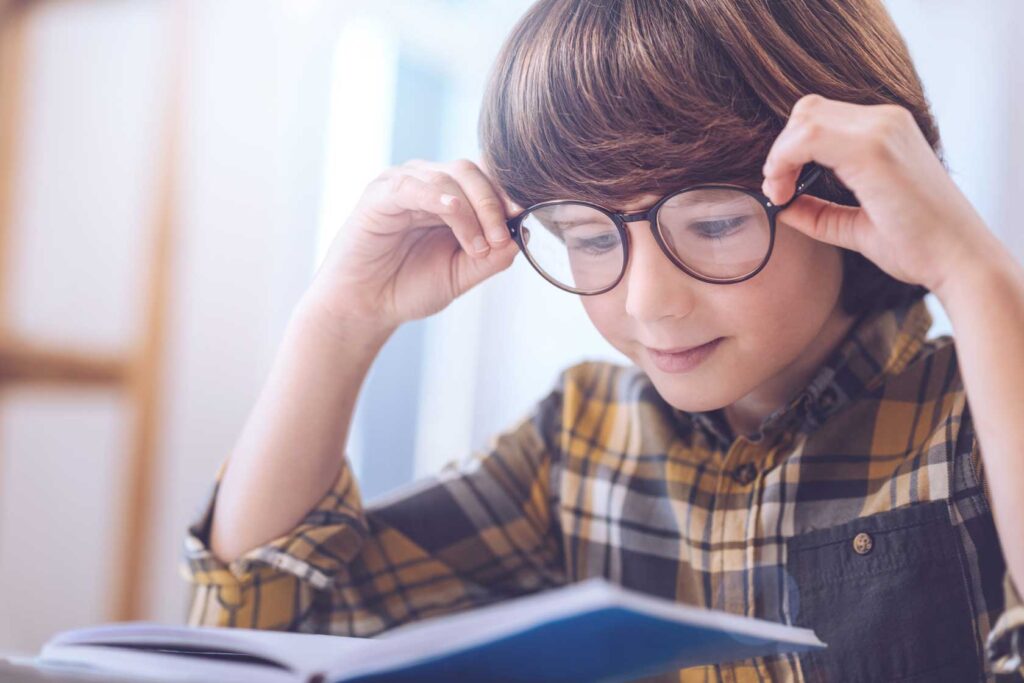 chłopiec w brązowych okularach nachylony nad książką, delikatnie się uśmiecha