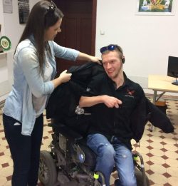 asystentka pomaga włożyć kurtkę mężczyżnie siedzącemu na wózku