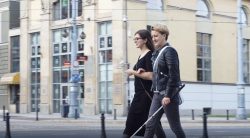 niewidoma kobieta z laską idzie ulicą, prowadzi ją asystentka